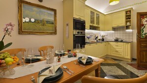 A dining area with a table set for four, a painting on the wall, and a kitchen in the background. - Charming Prague Downtown Flat (Prague)