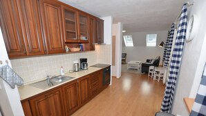A modern kitchen with wooden cabinets, a countertop with a coffee maker, and a dining area with a table and chairs. - Comfortable Apartment With Balcony, Storage and Parking (Nova Pec)