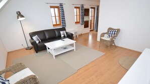 A spacious living area with a black leather sofa, white coffee table, wicker chairs, and a white table. - Comfortable Apartment With Balcony, Storage and Parking (Nova Pec)