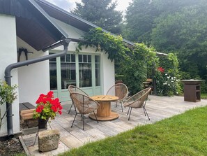 A patio with a table and chairs, a wooden bench, and a stone planter with red flowers.
