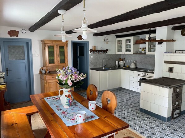 A kitchen with white cabinets, a wooden table with a floral tablecloth, and a blue door.