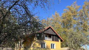 Une maison à deux étages avec un toit rouge, un balcon et un petit jardin.