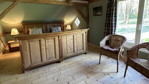 Une pièce avec un meuble en bois, deux fauteuils en osier, une fenêtre avec des rideaux et une lampe sur une table de chevet.