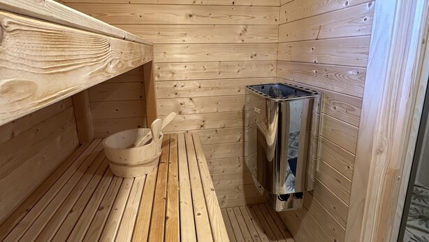 Un sauna en bois, avec un banc, un seau en bois et un appareil de chauffage pour sauna.