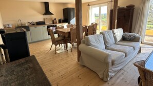 Eine Küche mit Herd, Spüle und Schränken, ein Essbereich mit Tisch und Stühlen sowie ein Wohnbereich mit Sofa und Vorhängen.