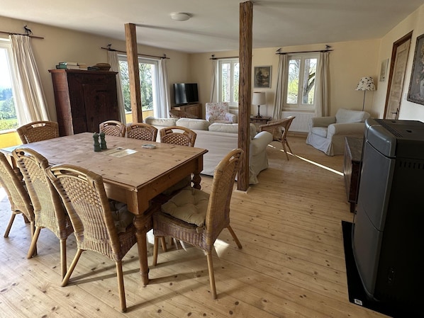 A spacious living area with a wooden dining table, wicker chairs, a sofa, and a television.