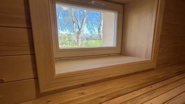 Eine Holzhütte mit einem Fenster mit Blick auf einen Wald.
