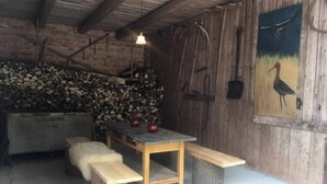 Een rustiek houten interieur met een houten tafel en banken, een hanglamp en een schilderij van een vogel aan de muur.