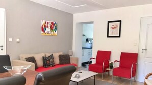 Een moderne woonkamer met een bank, rode stoelen, een salontafel en een eettafel.