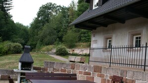 An outdoor patio with stone walls, wooden benches, and a barbecue grill. - Apartment in Bohemian With Shared Pool (Vidochov)