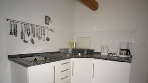 A compact kitchen with white cabinets, a granite countertop, a coffee maker, and various utensils hanging on the wall. - Apartment in Bohemian With Shared Pool (Vidochov)