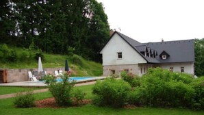 A house with a swimming pool, surrounded by a grassy lawn and dense trees. - Apartment in Bohemian With Shared Pool (Vidochov)