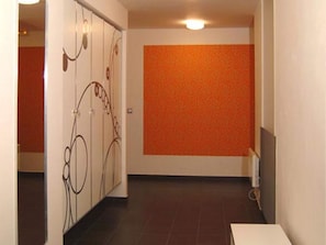 Ein Flur mit Fliesenboden, einer weißen Tür mit Dekor und einer orangefarbenen Wand mit Struktur.