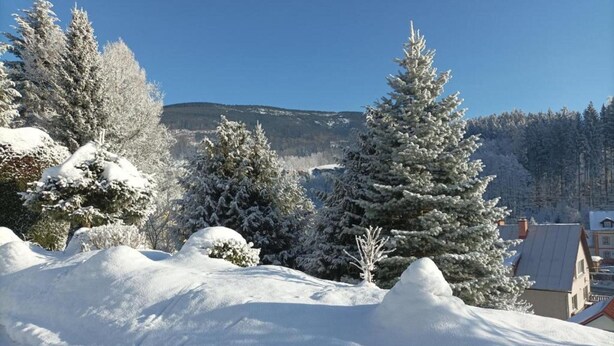 A snow-covered landscape with a mountain in the background and a building with a sloped roof. - Attractive Apartment in Rokytnice nad Jizerou near Ski Area (Rokytnice nad Jizerou)