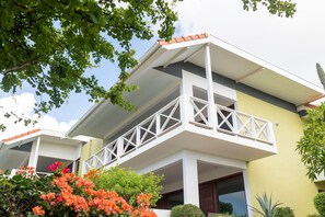 A modern two-story building with a balcony, surrounded by greenery and flowering plants. - Luxurious Apartment in Jan Thiel With Pool (Jan Thiel)