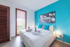 A bedroom with a bed, a painting of flamingos, a nightstand with a lamp, and a window with blinds. - Luxurious Apartment in Jan Thiel With Pool (Jan Thiel)