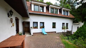 Une maison à deux étages avec un patio, une table en bois et une chaise bleue.