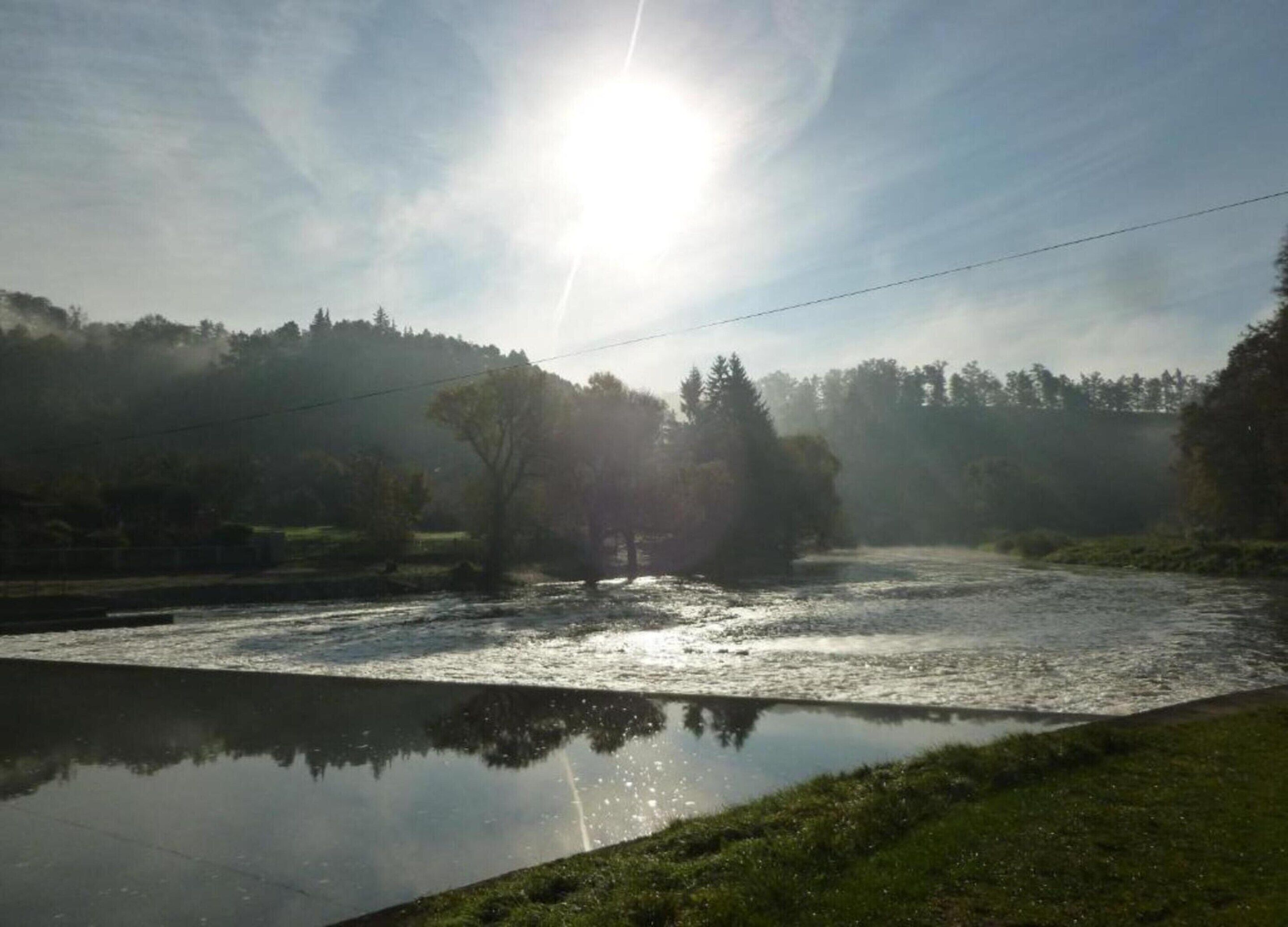 Une rivière dont l’eau reflète clairement les arbres, avec une ligne électrique qui la surplombe.