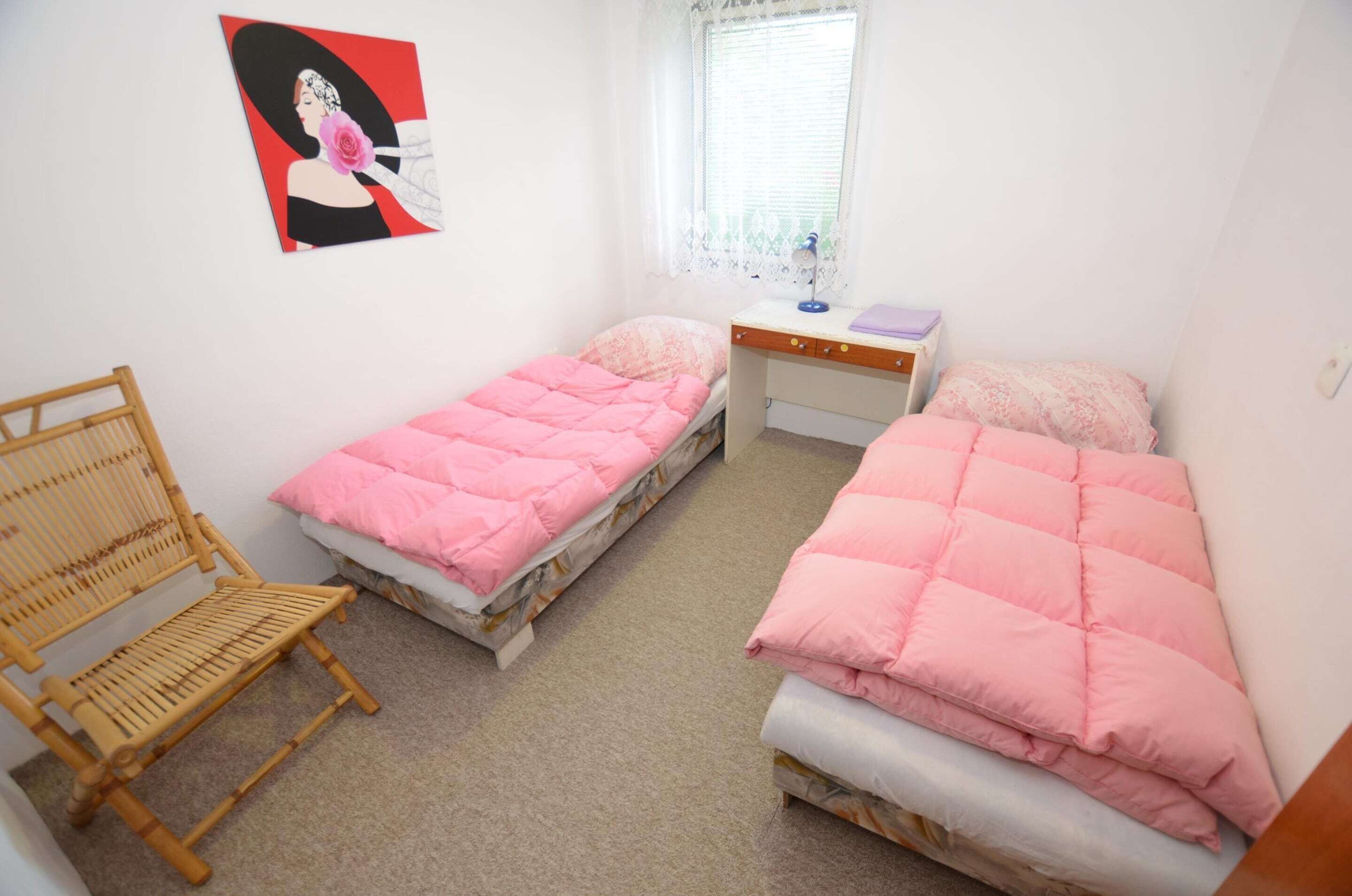 A bedroom with two single beds, a desk, a chair, and a window with lace curtains.
