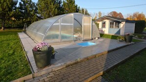 Un invernadero con techo transparente, una pequeña piscina y una casa al fondo.