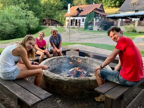 A group of people around a campfire in a backyard with a house and a wooden deck in the background. - Mansion in Starkov Near Acitvities (Starkov)