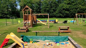 A playground with a wooden playhouse, slides, swings, and picnic tables.