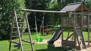 A playground with a wooden swing set, a slide, and a small wooden structure.