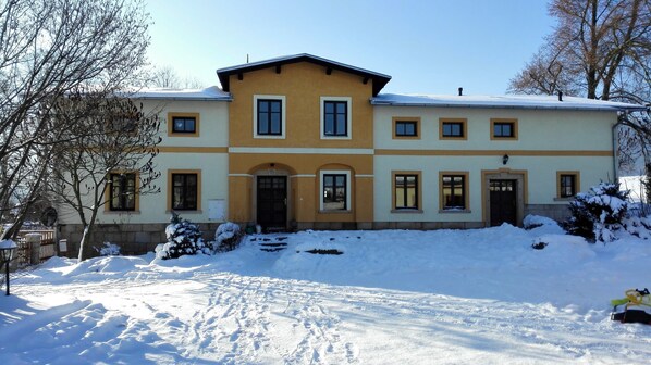 Un edificio de dos pisos con fachada simétrica, ventanas amplias y suelo cubierto de nieve.