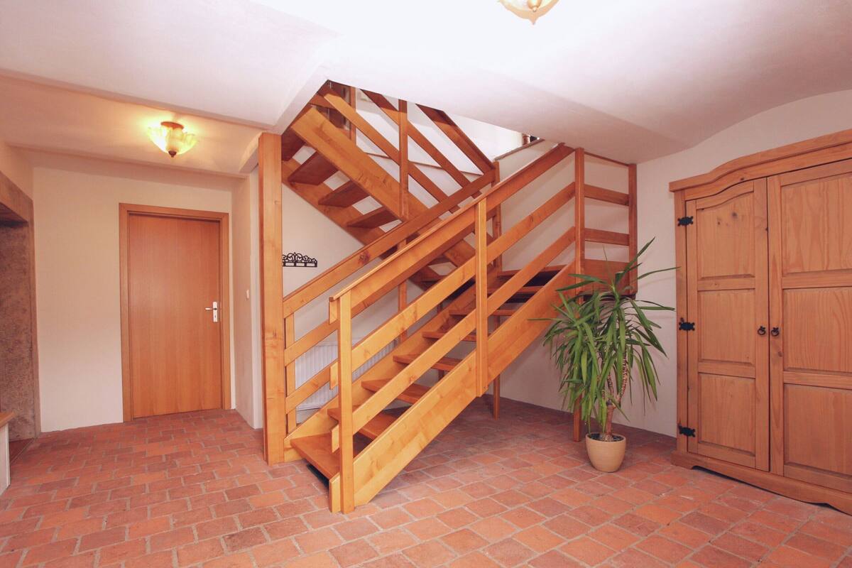 Una escalera de madera en una habitación con suelo de baldosas, una puerta, un armario y una planta en maceta.