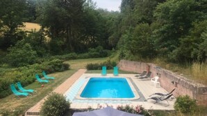 Une piscine rectangulaire dont le bord est recouvert de carreaux, entourée d’un mur de briques et d’une pelouse agrémentée de chaises longues.