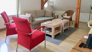 Un salon chaleureux avec un canapé, deux fauteuils rouges, une table basse en bois et une lampe.
