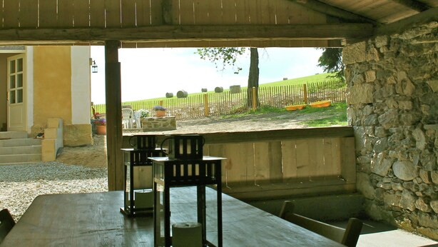 An outdoor covered patio with a stone wall, wooden table, and chairs. - Holiday Home Milire Bohemian Forest (Milire)