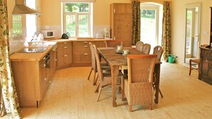 A spacious kitchen with wooden cabinets, a dining table with wicker chairs, and a view of the garden through the windows. - Holiday Home Milire Bohemian Forest (Milire)