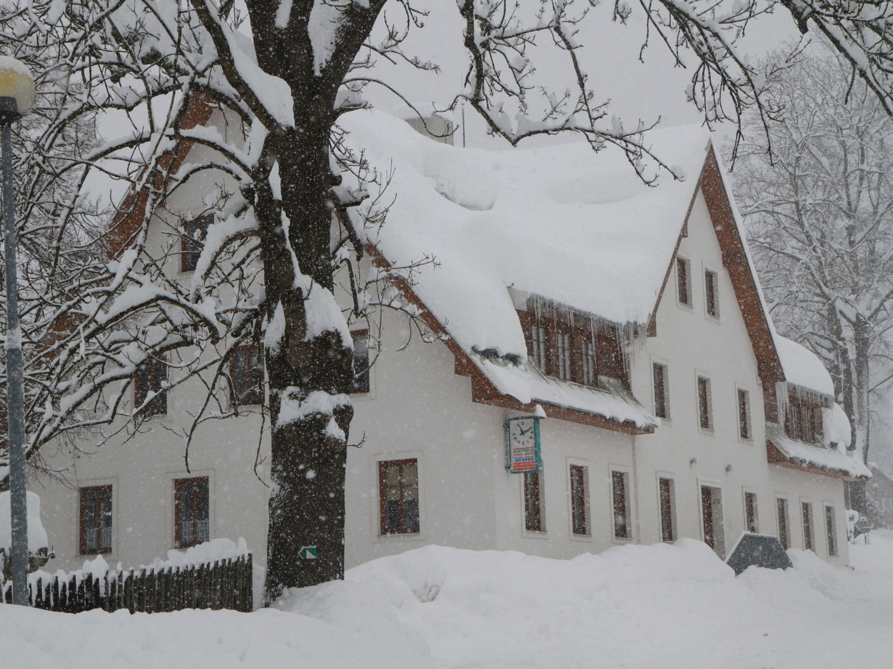 A snow-covered building with a traditional architectural style, featuring multiple windows and a steeply pitched roof.