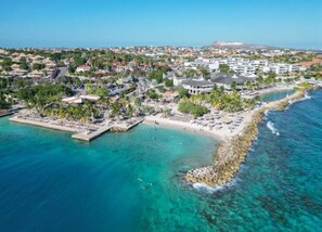 An aerial view of a coastal resort with a beachfront, a marina, and a variety of buildings including hotels and villas.