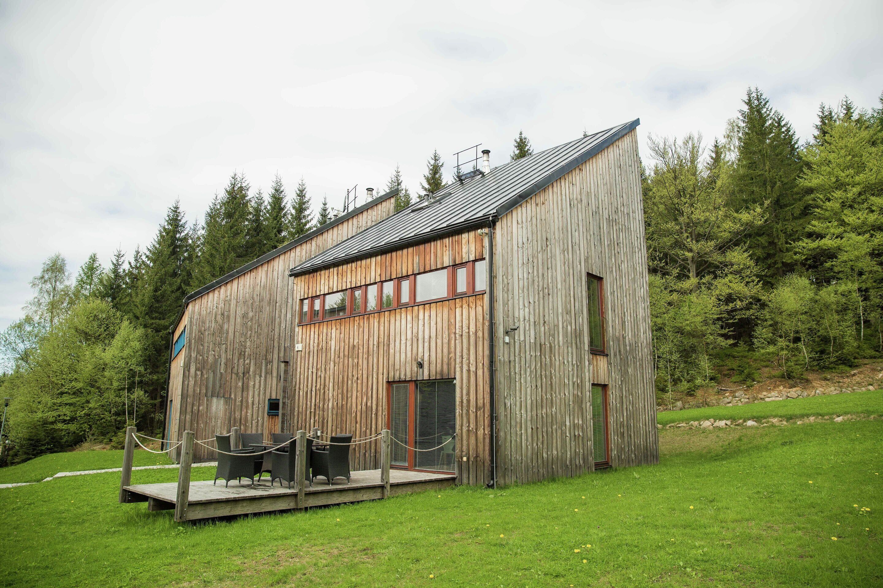 A rustic wooden cabin with a deck, surrounded by a forest.