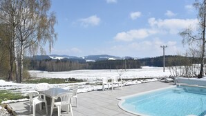 Un espace piscine avec une table et des chaises, entouré d’un paysage enneigé et d’arbres.