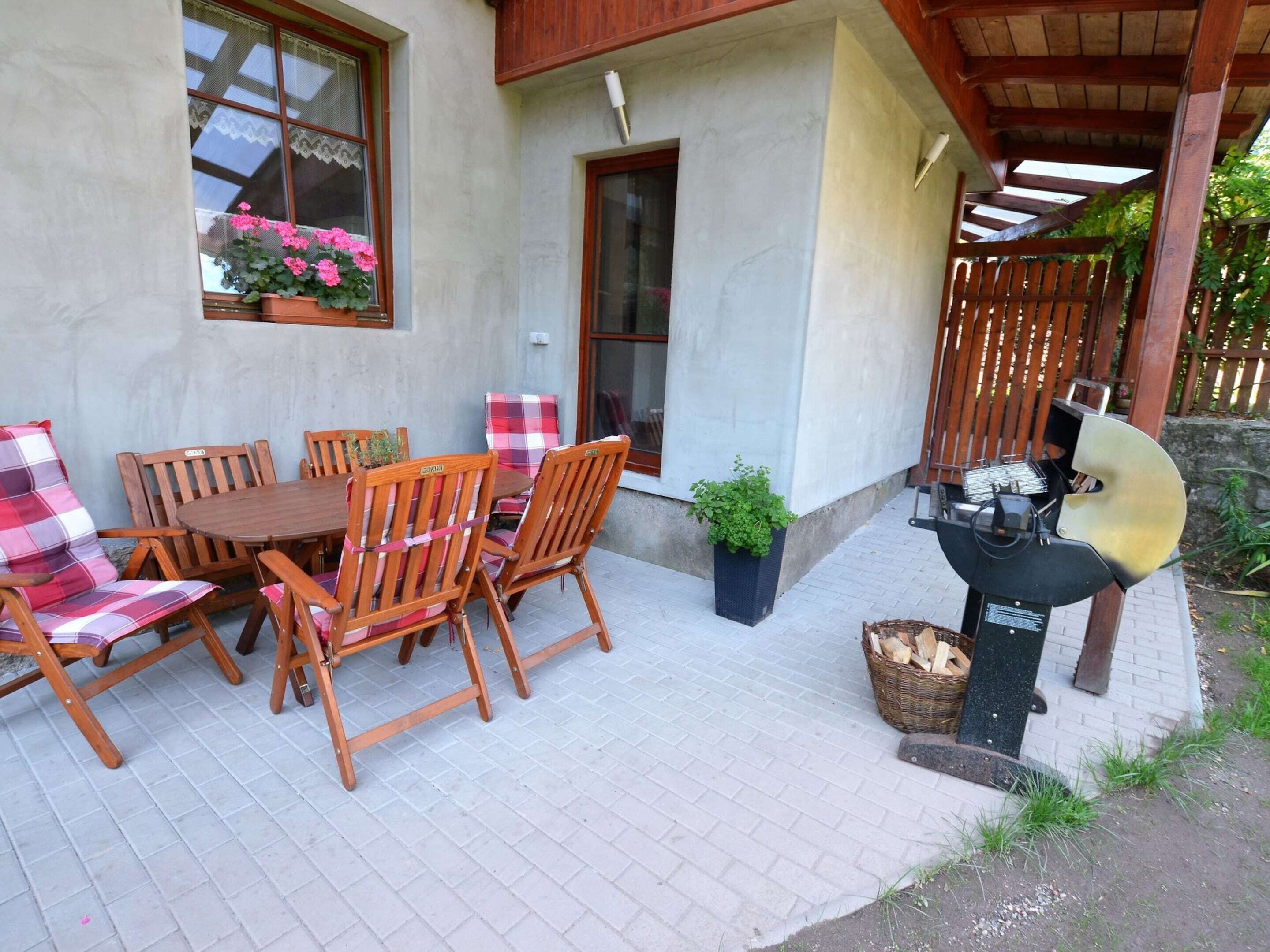 An outdoor patio with a wooden table and chairs, a grill, and potted plants.
