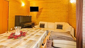 A cozy cabin room with a wooden interior, a television mounted on the wall, a sofa, a dining table with a checkered tablecloth, and a glass vase with red berries. - Mountain Home With Garden (Cerny Dul)