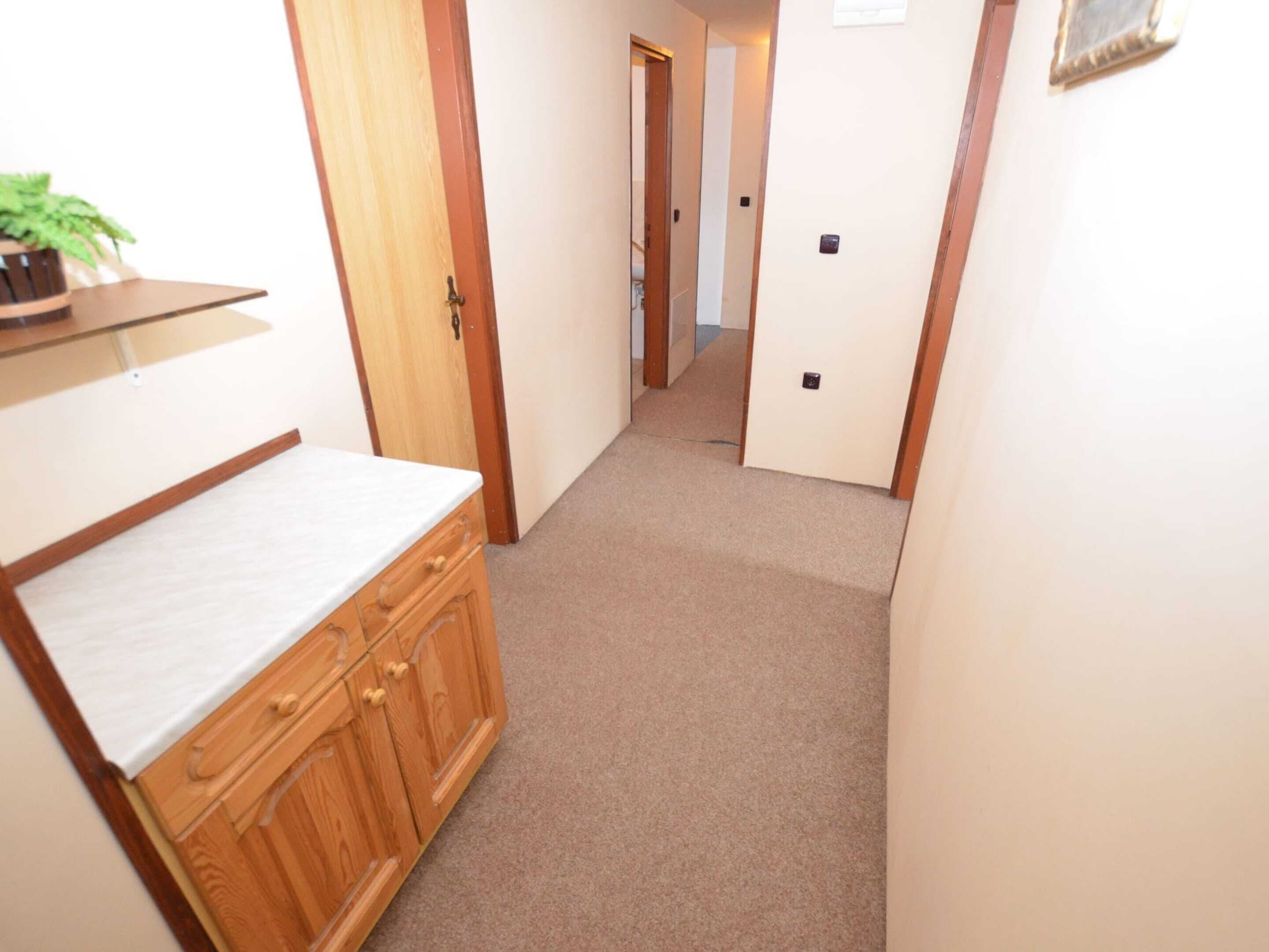 A narrow hallway with a wooden cabinet and a small shelf with a plant.