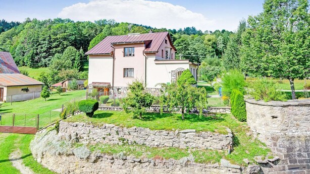 A two-story house with a stone wall in the foreground and a metal fence. - Mountain Home With Garden (Cerny Dul)