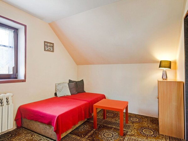 A small, cozy room with a bed, a small table, a lamp, and a radiator.