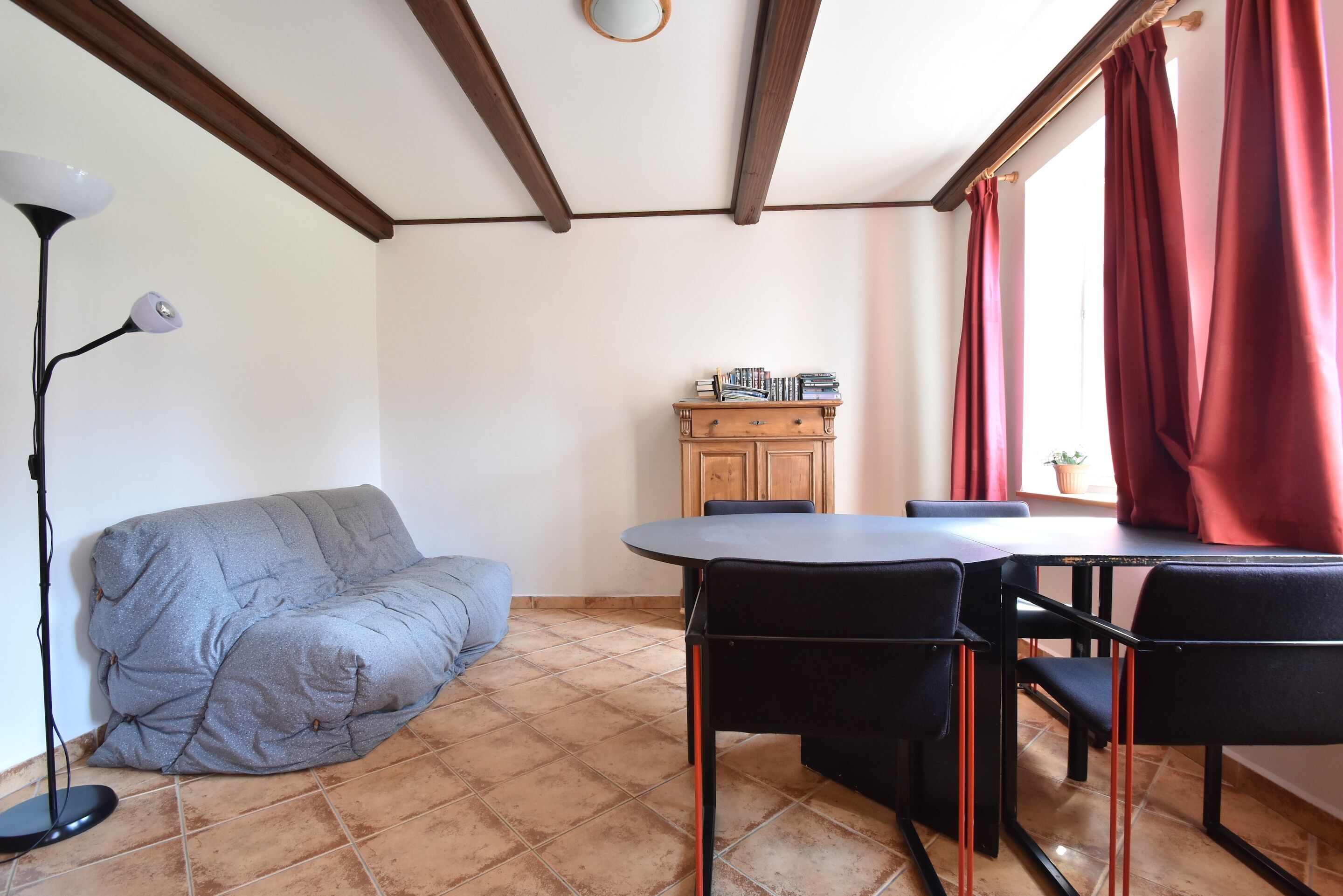 A room with a sofa, a dining table with chairs, a floor lamp, and a cabinet with books.