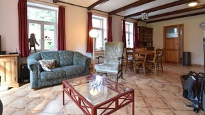 A living room with a sofa, armchair, and glass coffee table, wooden beams on the ceiling, and a dining area with chairs and a table. - Holiday Home Rudnik Near Ski Lift (Rudník)