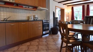 A kitchen with wooden cabinets, a tiled backsplash, a stove, and a dining area with chairs and a table. - Holiday Home Rudnik Near Ski Lift (Rudník)