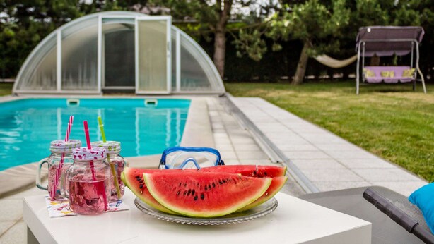 A poolside setting with a swimming pool, a covered area, and a hammock.