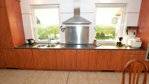 A kitchen with wooden cabinets, a stainless steel range hood, a sink, and a window overlooking greenery.