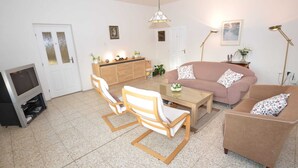 A living room with a sofa, two armchairs, a coffee table, a TV, a cabinet, and a door.