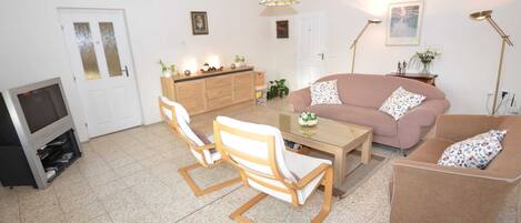 A living room with a sofa, two armchairs, a coffee table, a TV, a cabinet, and a door.