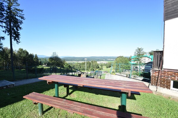 Una mesa de picnic con bancos en un área verde con vistas a colinas distantes y un parque infantil.